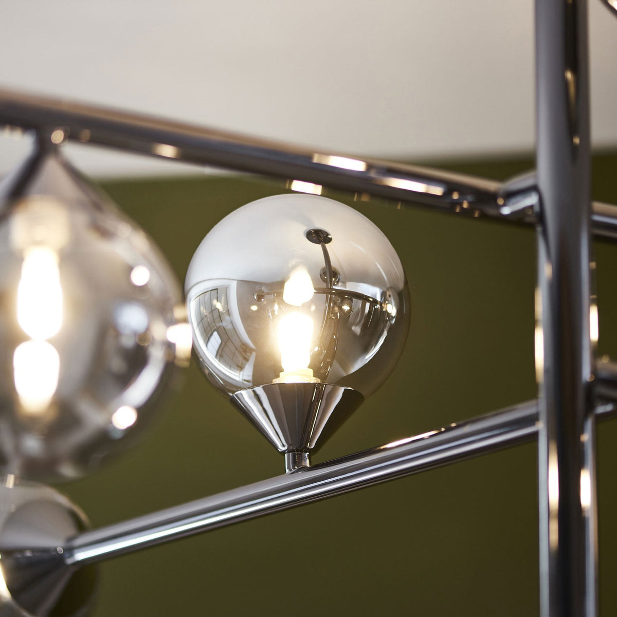 Extreme close-up of a spherical smoked glass shade with a visible glowing bulb on a chrome chandelier.