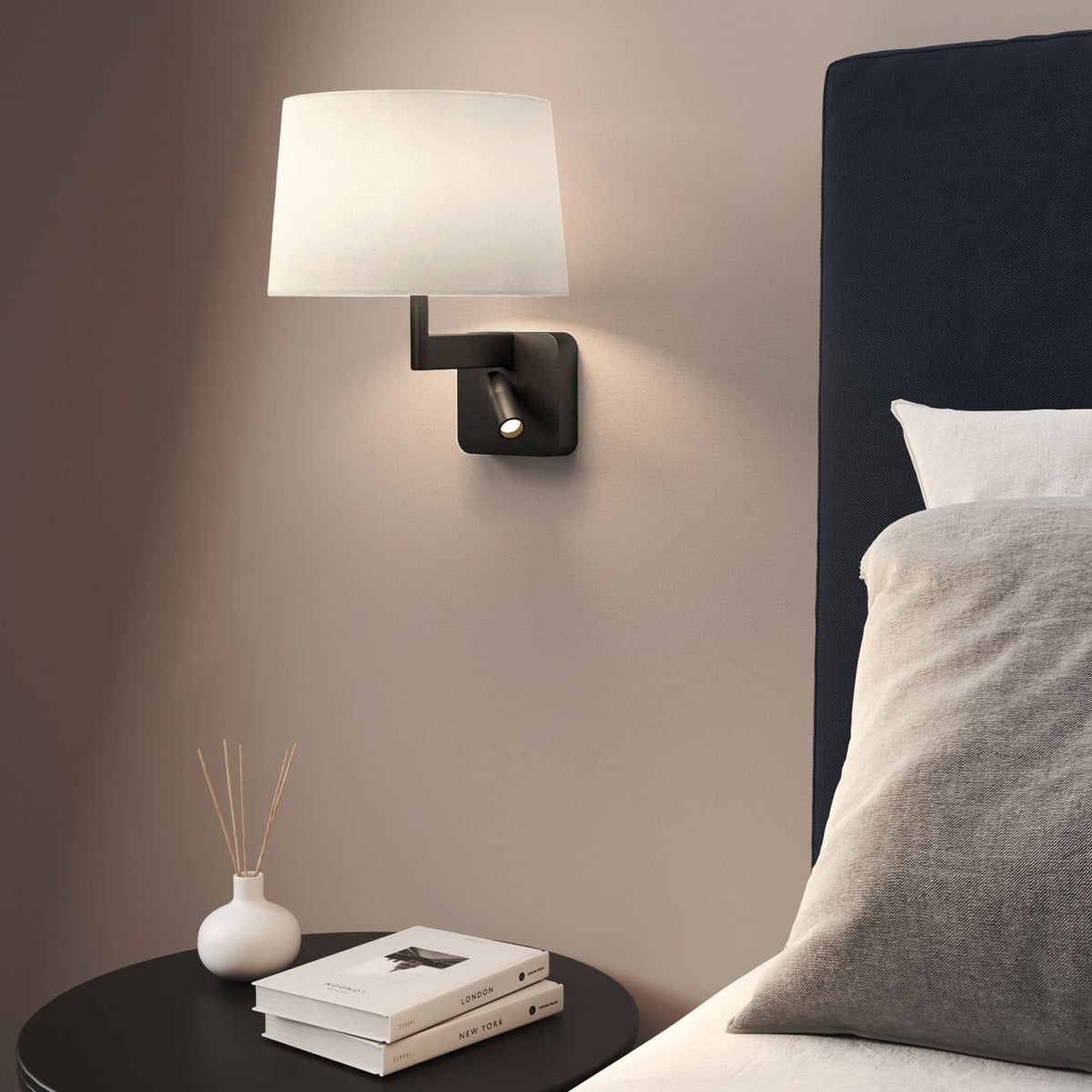 Wall-mounted lamp with white shade and adjustable reading light above a black side table