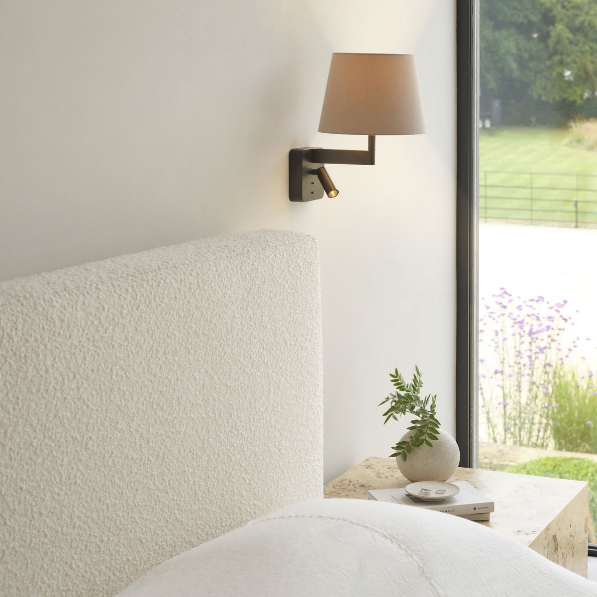 Wall-mounted lamp with a fabric shade and a directional reading light above a textured headboard