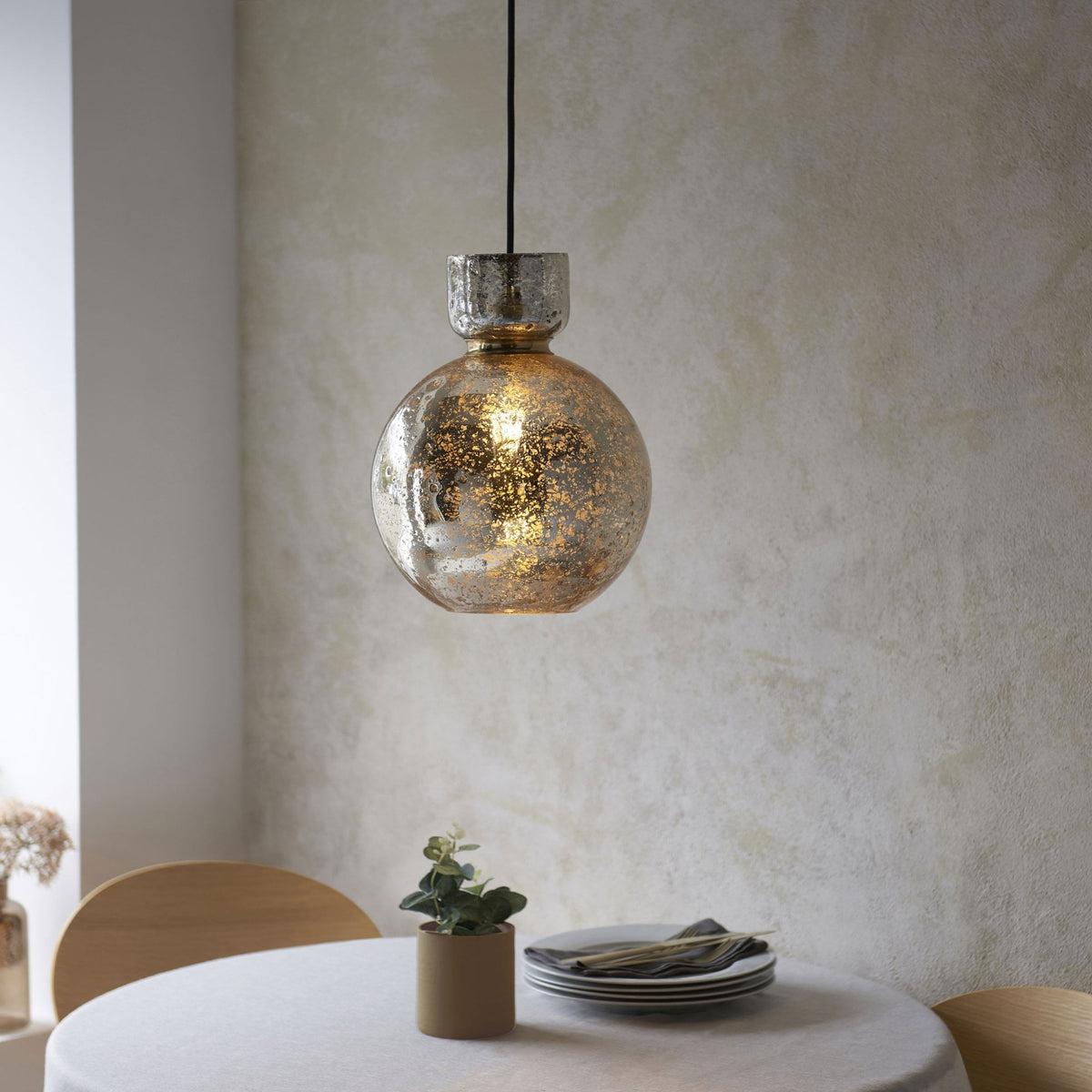 A round, textured glass pendant light hangs over a dining table set for a meal, illuminated by a warm glow.