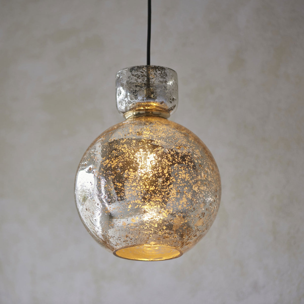 A round, speckled glass pendant light casting a warm, inviting glow over a room with muted tones.