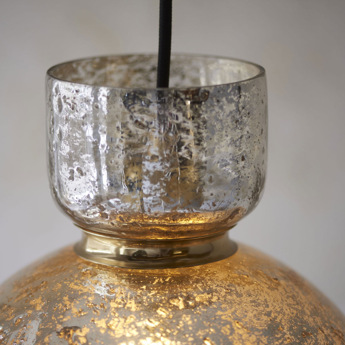 Close-up of the upper portion of a mercury glass pendant light, showing the silver textured top and gold rim.