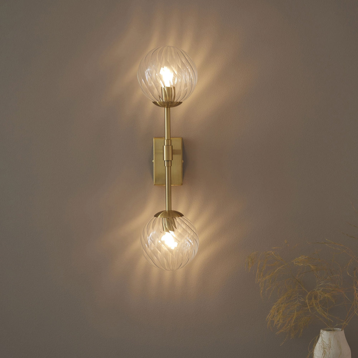 Une applique murale dorée élégante avec deux abat-jour sphériques en verre texturé, émettant une lumière chaude et ondulante.
