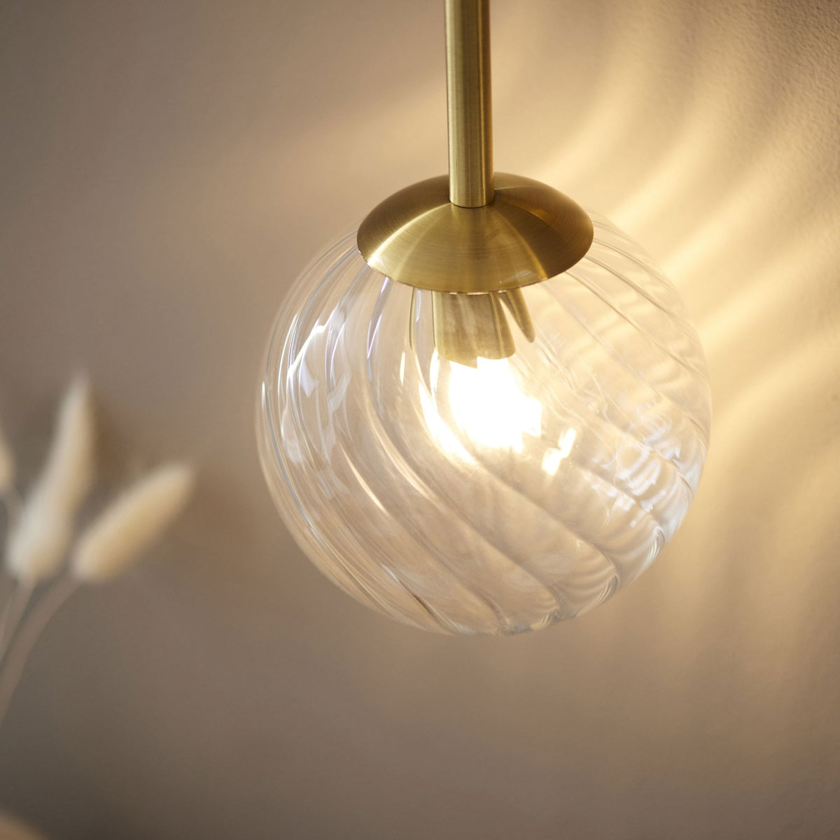 Gros plan d'un abat-jour sphérique en verre texturé, émettant une lumière chaude sur le mur derrière.
