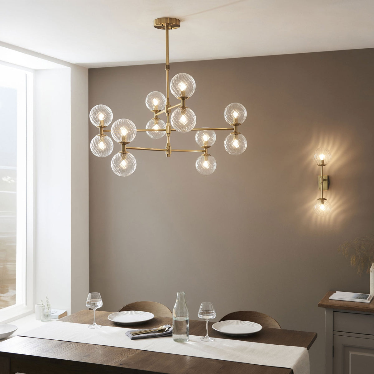 Une salle à manger moderne avec un lustre doré et une applique murale assortie, éclairant une table dressée.
