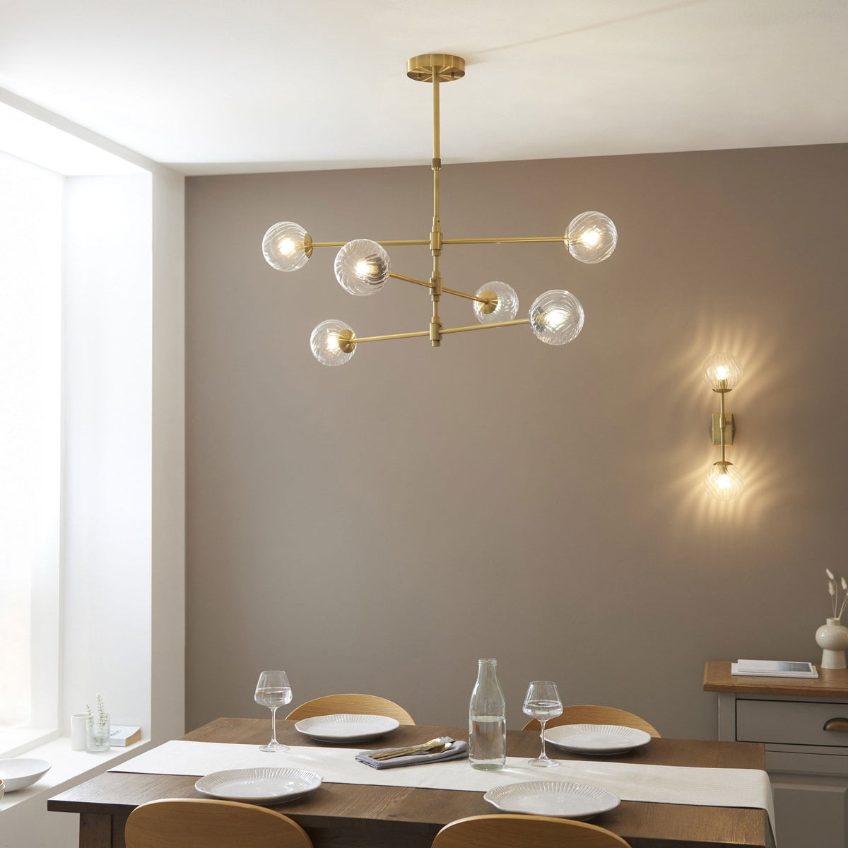 Lustre et applique murale dorés modernes avec des globes en verre, éclairant une salle à manger élégante et neutre.