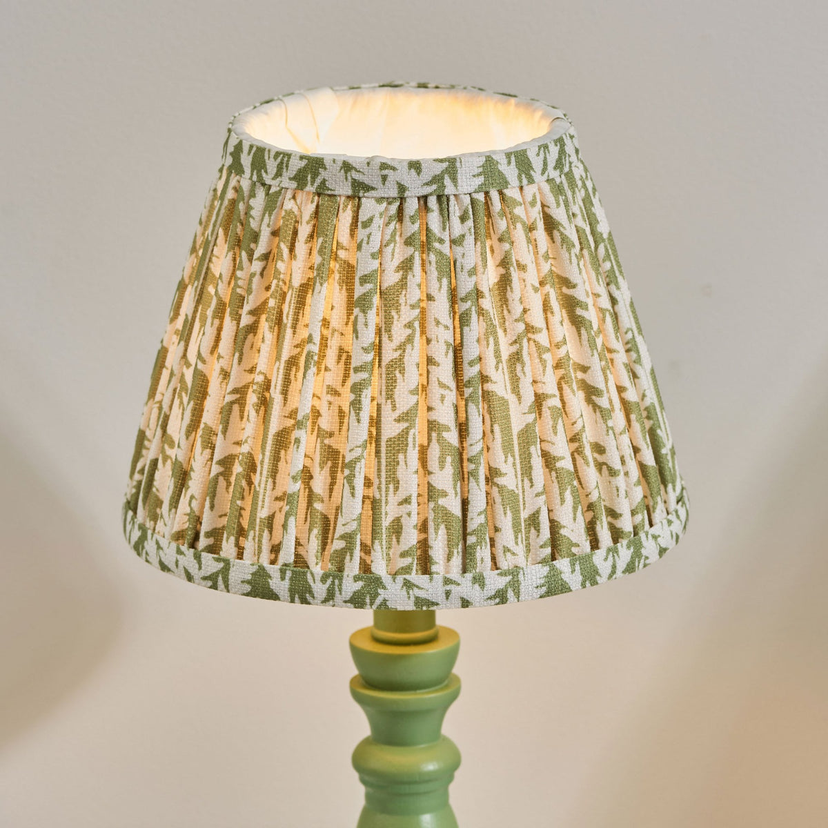 A close-up of a lit patterned fabric lamp shade on a green wooden base.
