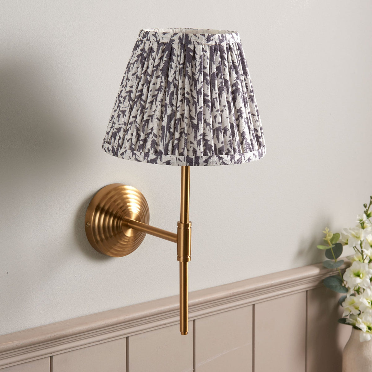 A brass wall light with a grey and white patterned pleated lampshade.