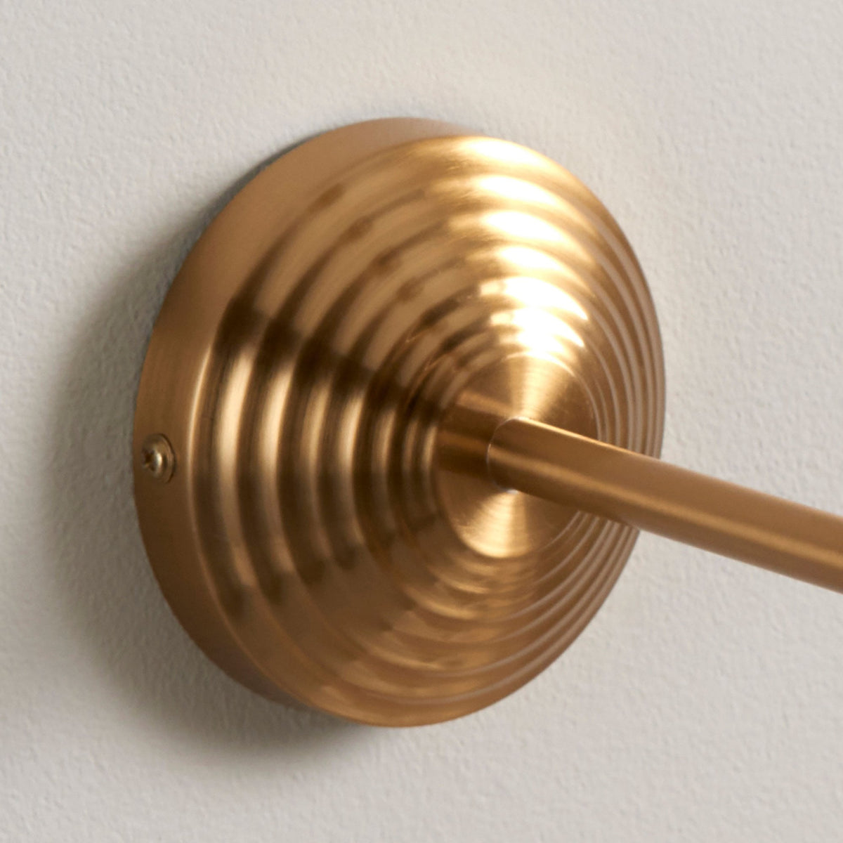 Close-up of the ribbed, round brass wall mount of the wall light.