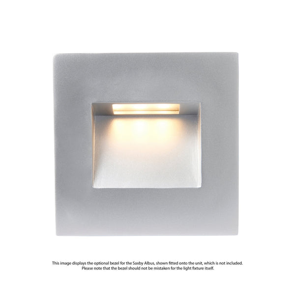 A square, silver-coloured recessed wall light with a warm yellow glow from its opening.