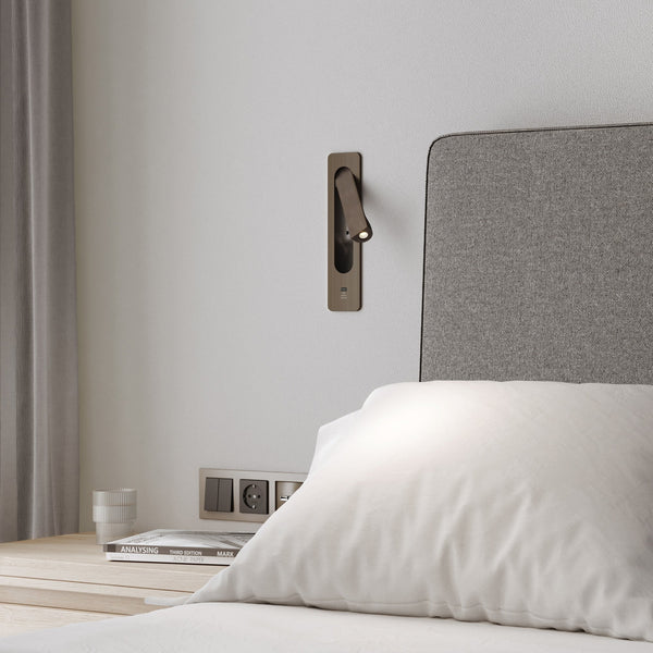A modern bedroom with a wall-mounted reading light, a grey upholstered headboard, and a wooden nightstand