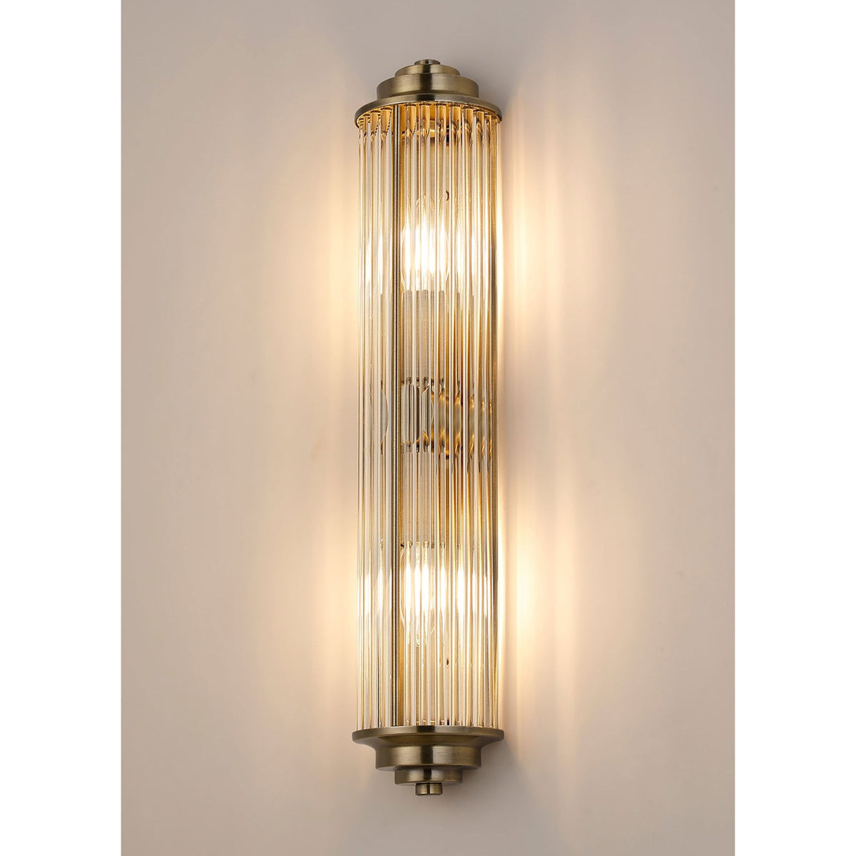 An ornate brushed brass reeded glass wall light with two bulbs against a cream background.
