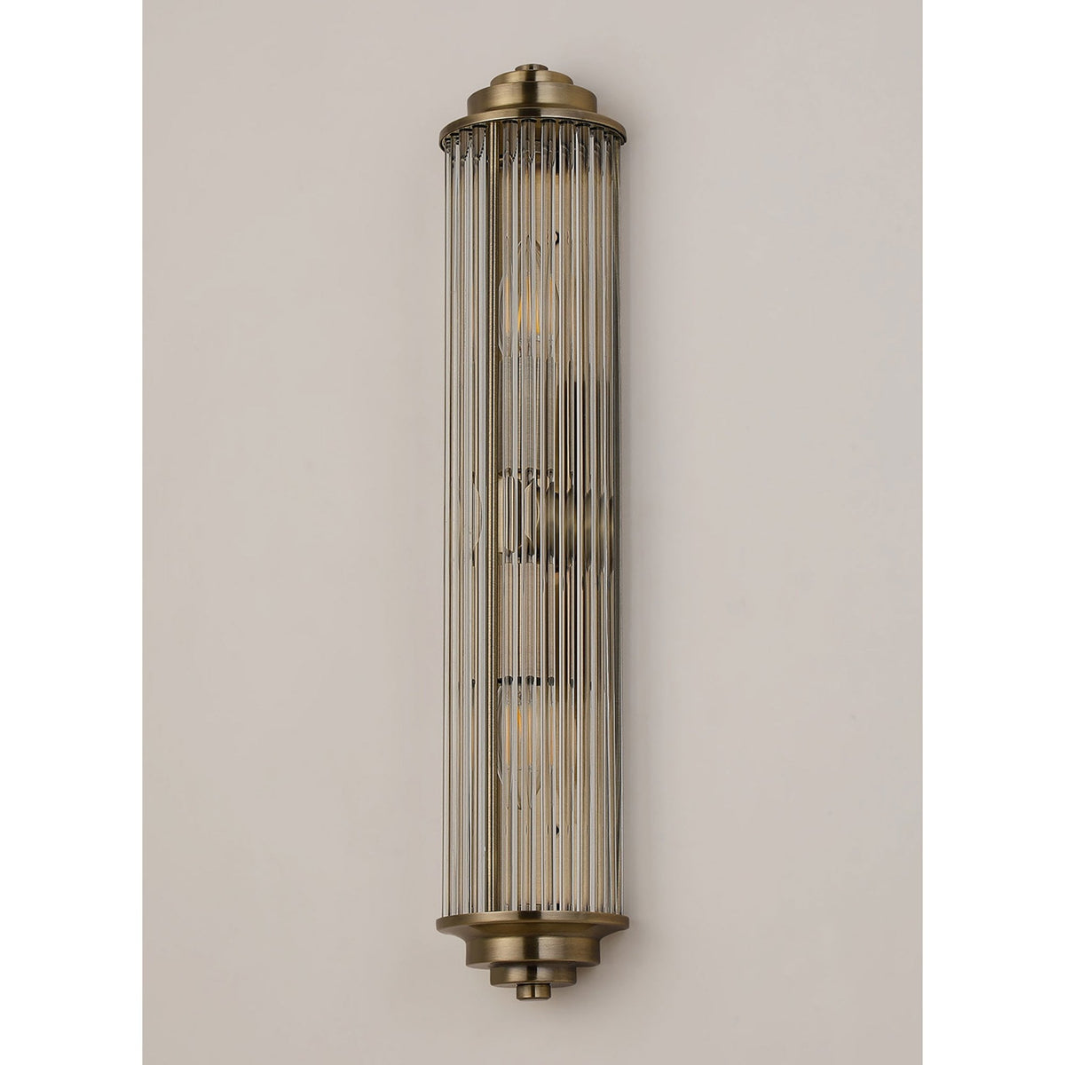 An ornate brushed brass reeded glass wall light with no illumination against a cream background.