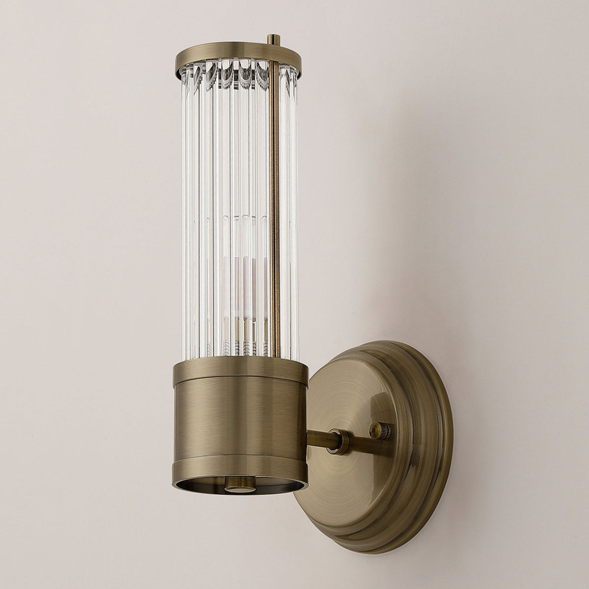 A brass wall light with a fluted glass cylinder shade, unlit, against a light wall.