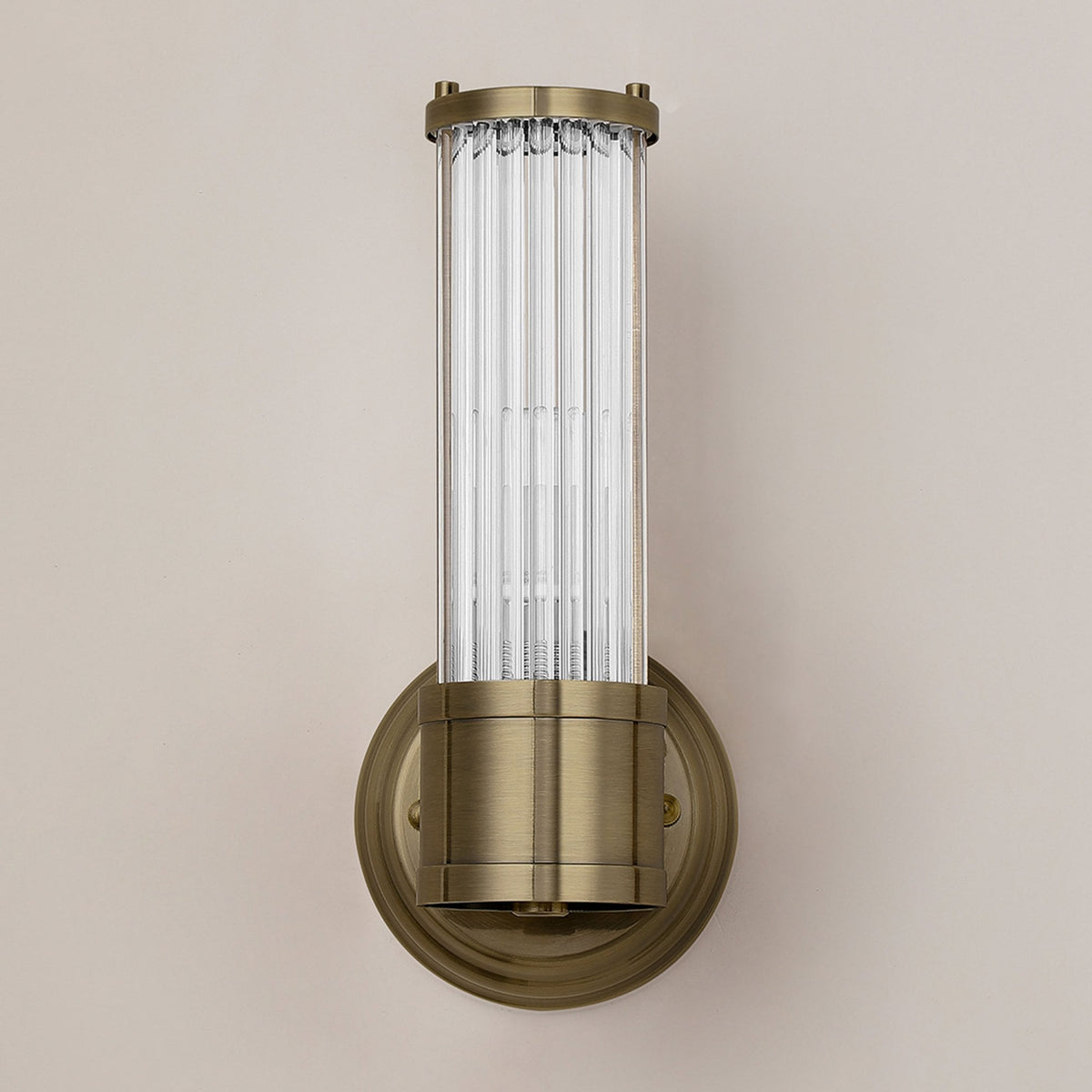 A front view of a brass wall light with a fluted glass cylinder shade, unlit.