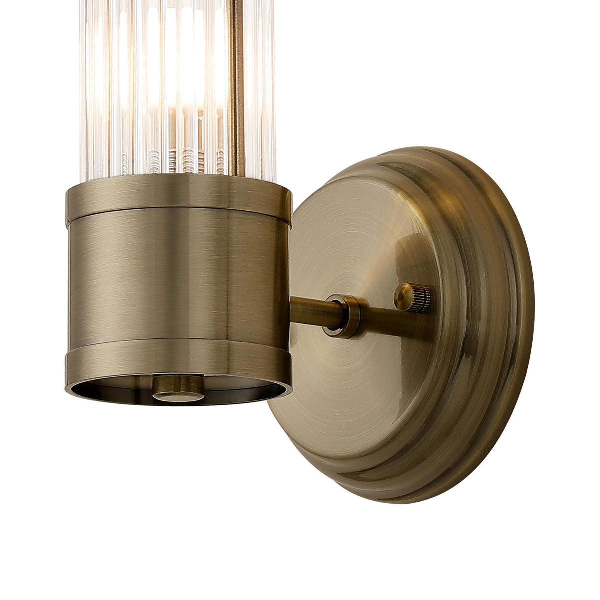 A close-up of the base of a brass wall light with a fluted glass cylinder shade.