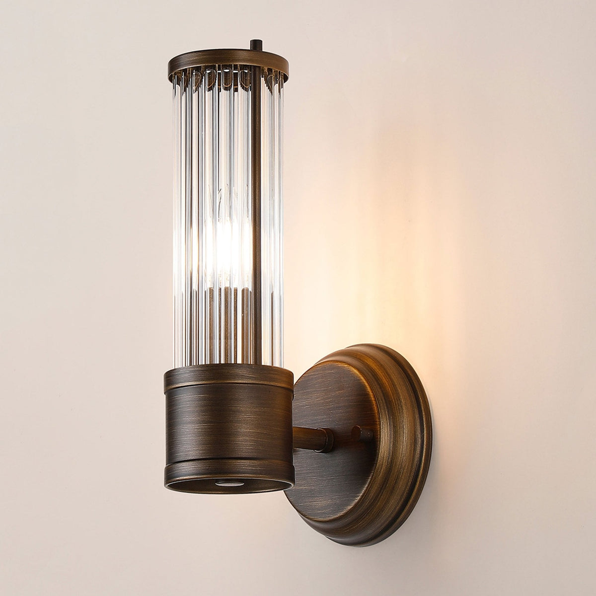 A close up of a lit ribbed clear glass wall light against a beige wall.