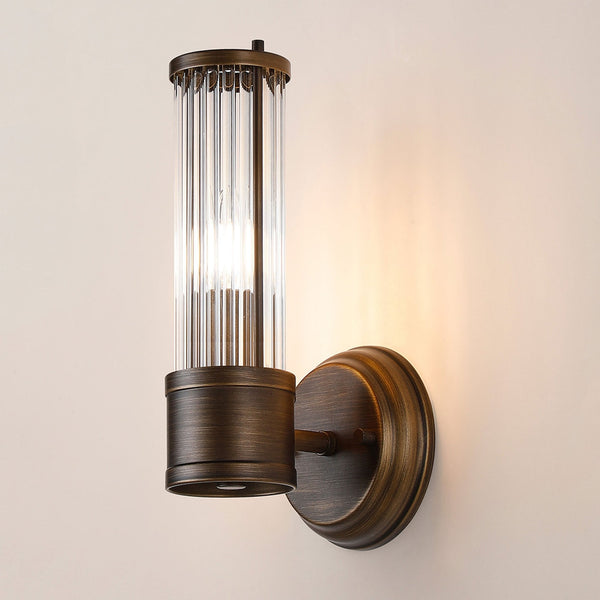 A close up of a lit ribbed clear glass wall light against a beige wall.