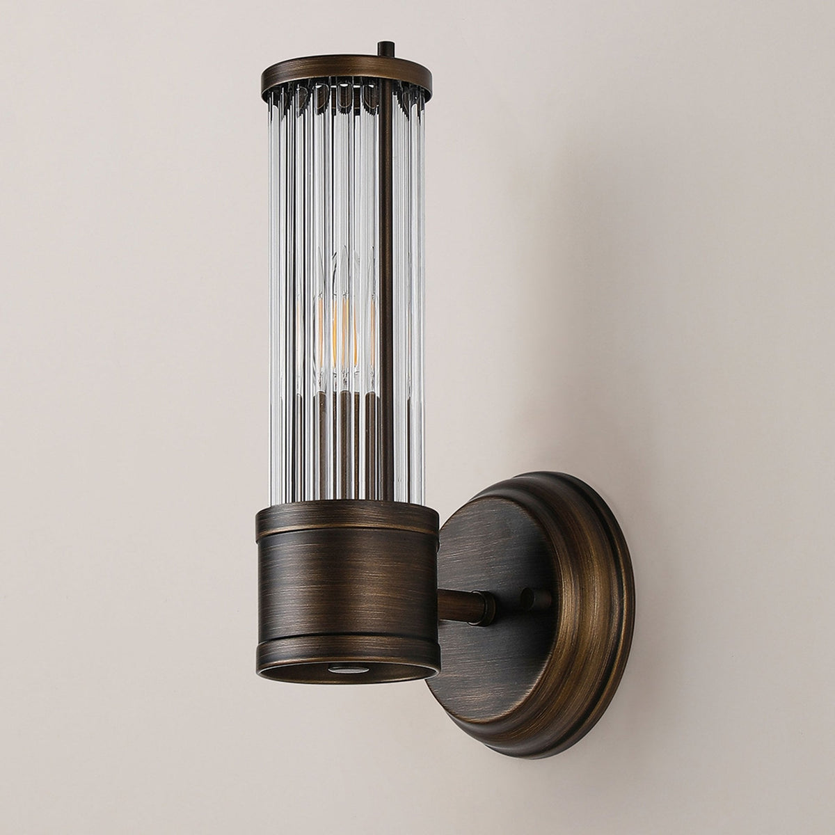 A close up of a lit ribbed clear glass wall light against a beige wall.