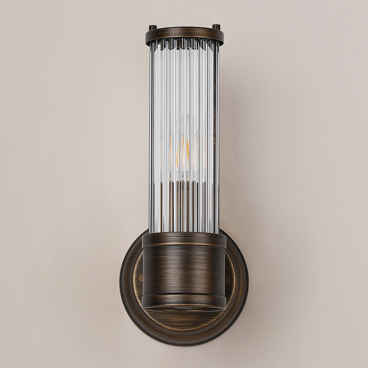 A close up of an unlit ribbed clear glass wall light against a beige wall.