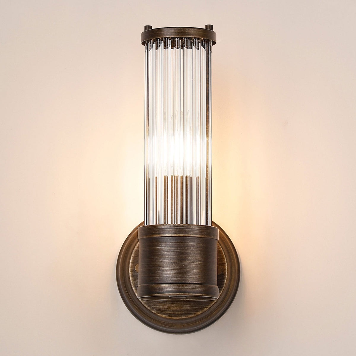 A close up of a lit ribbed clear glass wall light against a beige wall.