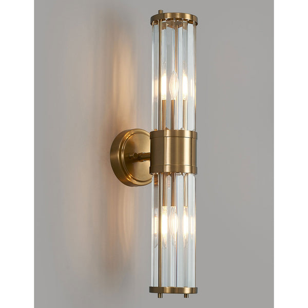 A modern brass and fluted glass wall light on a light grey wall, glowing.