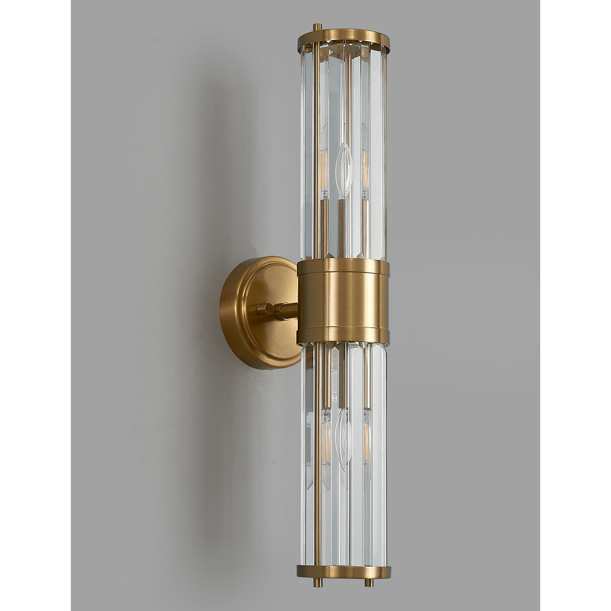 A modern brass and fluted glass wall light with unlit bulbs on a medium grey wall.