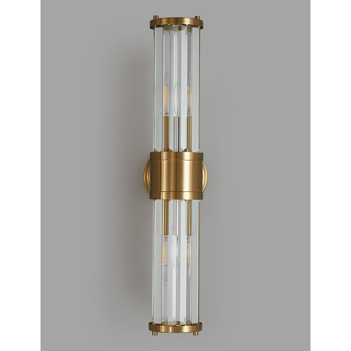 A modern brass and fluted glass wall light with unlit bulbs on a medium grey wall, front view.