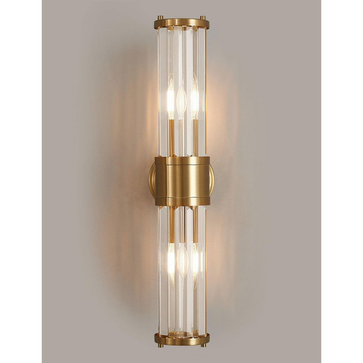A modern brass and fluted glass wall light on a medium grey wall, glowing.