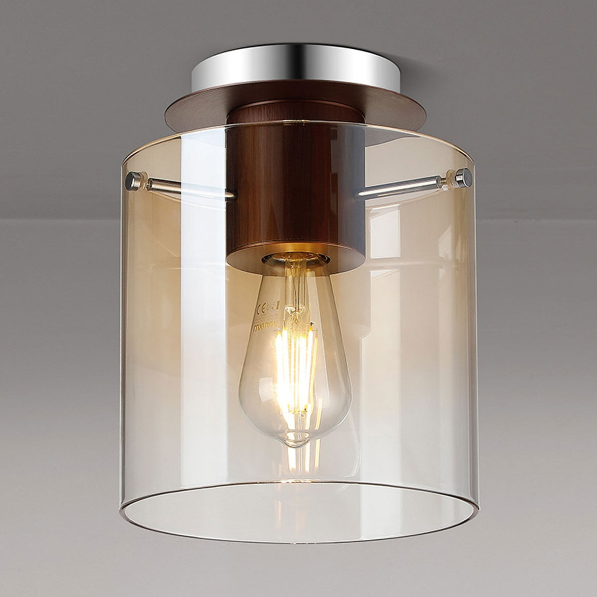 A close-up of a ceiling light featuring a clear, cylindrical amber-tinted glass shade.