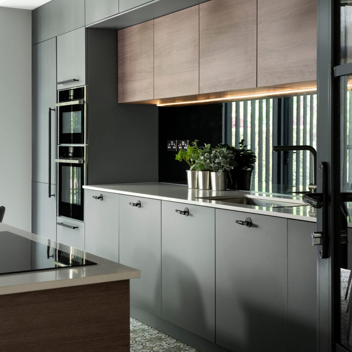Modern kitchen with grey cabinets, wooden upper cabinets, built-in ovens, and a kitchen island