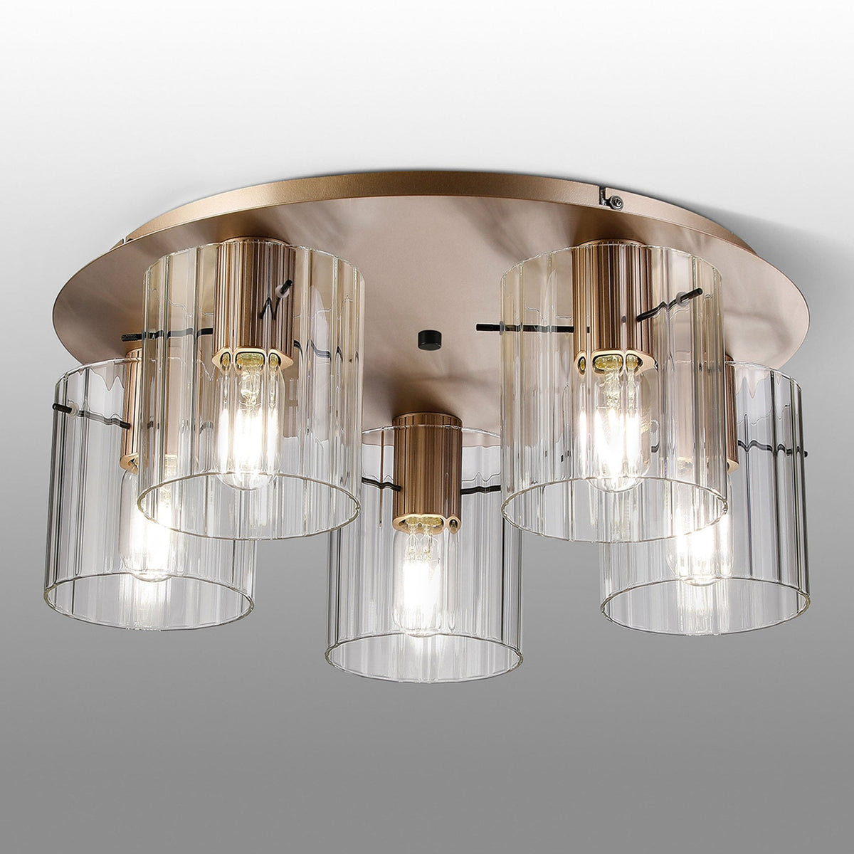 A modern brass ceiling light with five fluted glass shades on a grey background.