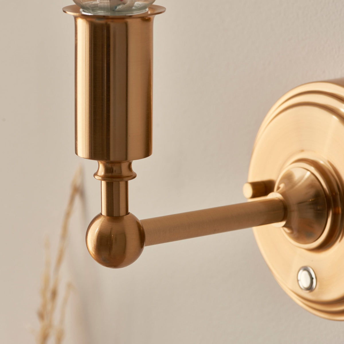Close-up of a brass wall sconce arm extending from a round wall plate.