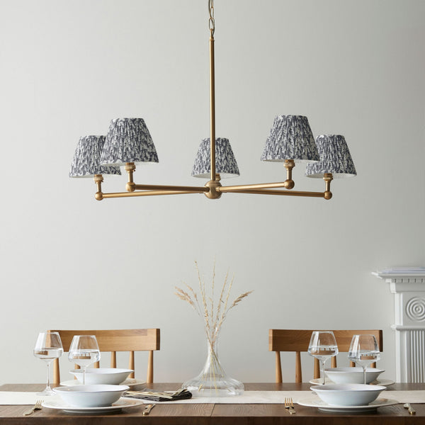 A dining table set for dinner with a brass chandelier overhead with five patterned shades.