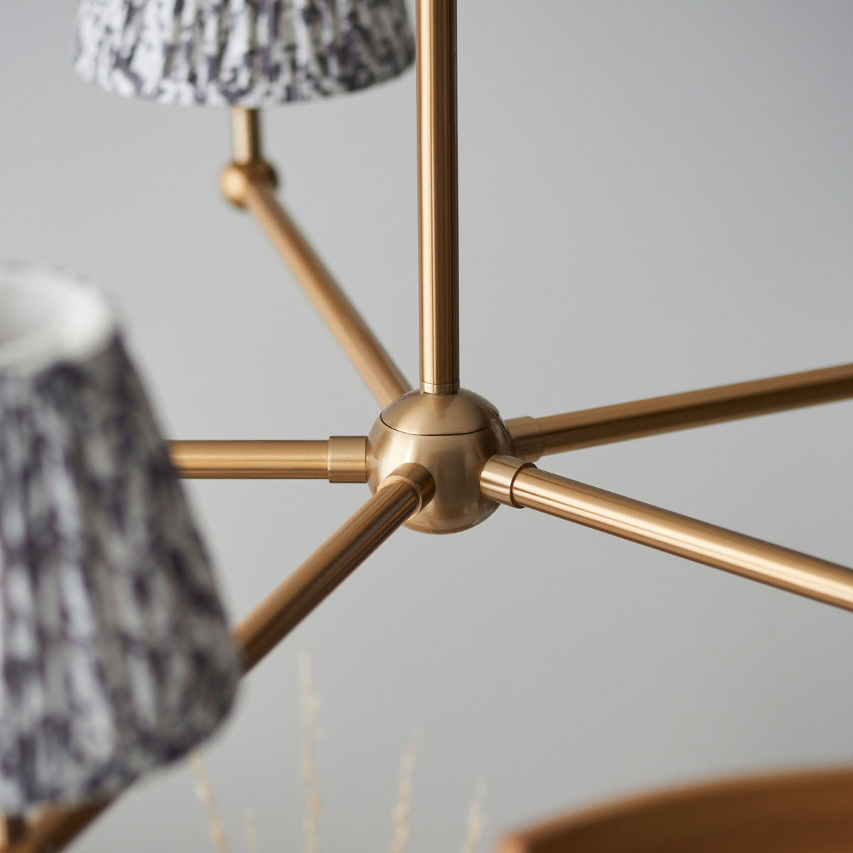 A close-up of the brass chandelier's central joint and arms with two patterned shades visible.