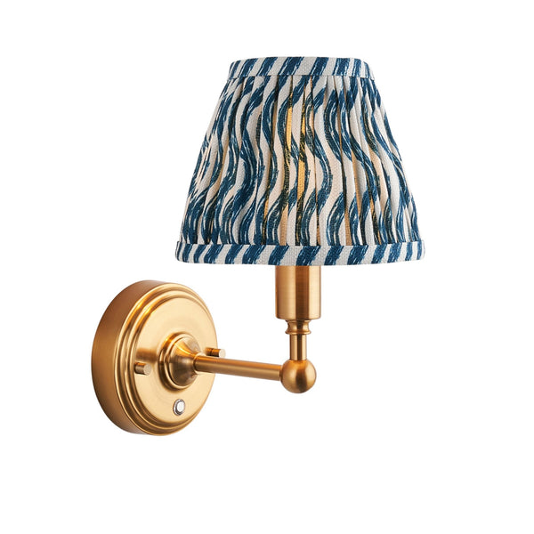 A brass wall light with a blue and white patterned pleated shade on a white background.