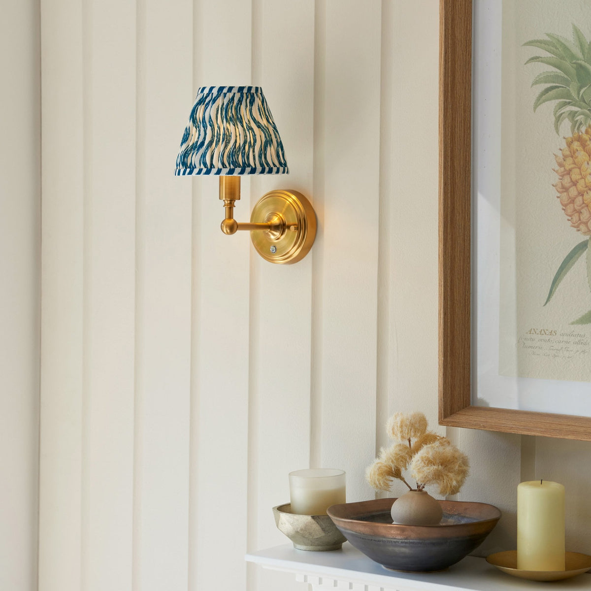 A brass wall light with a blue and white patterned pleated shade above decorative items.