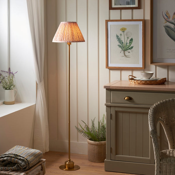 A brass floor lamp with a pleated, patterned lampshade, illuminating a room with soft light.
