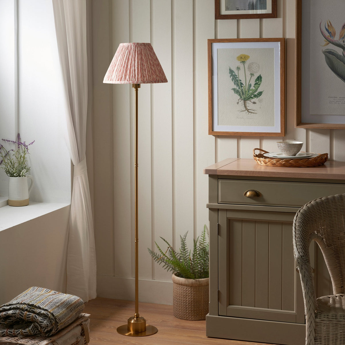 A brass floor lamp with a pleated, patterned lampshade in a cosy living room setting.