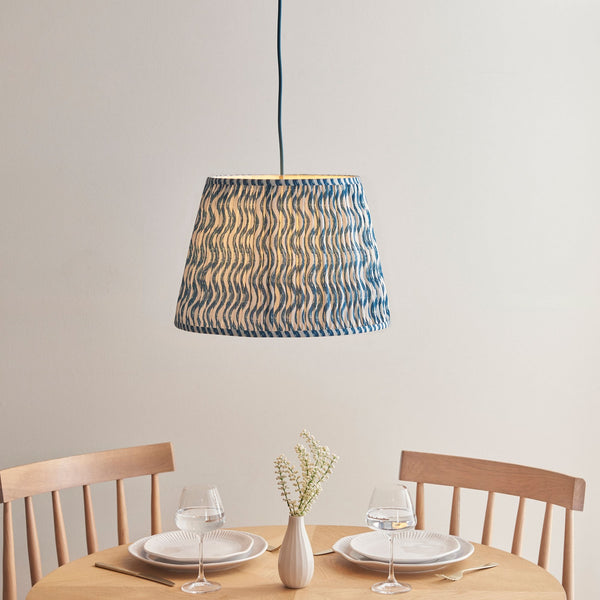 A blue and white wavy patterned lampshade hanging above a dining table set for two.