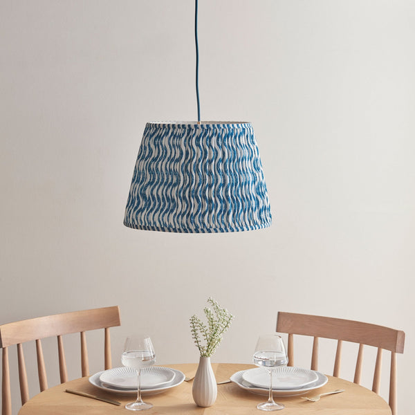 A pleated blue and white patterned lampshade hanging over a dining table set for two.
