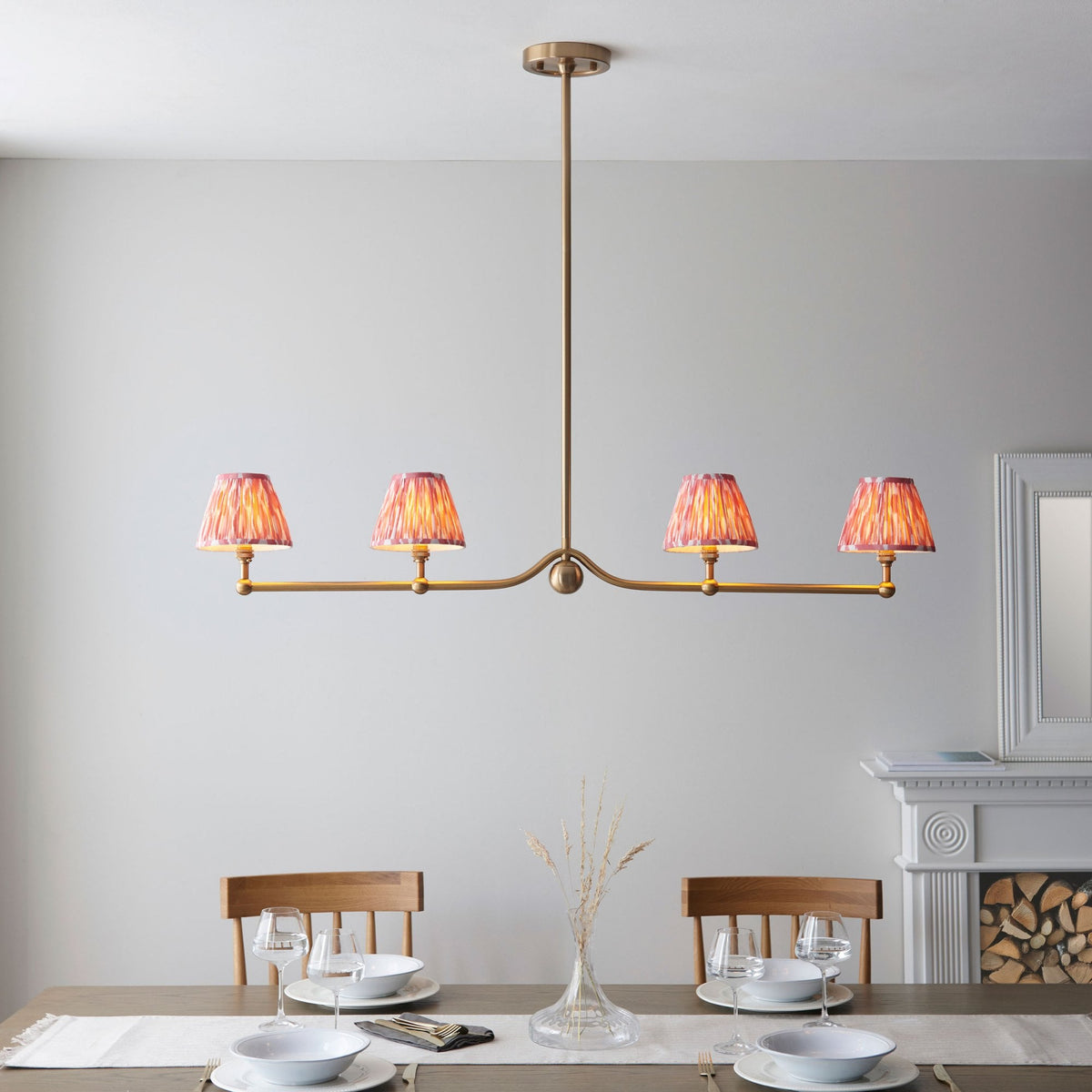 A four-light pendant with red pleated shades above a dining table with place settings.