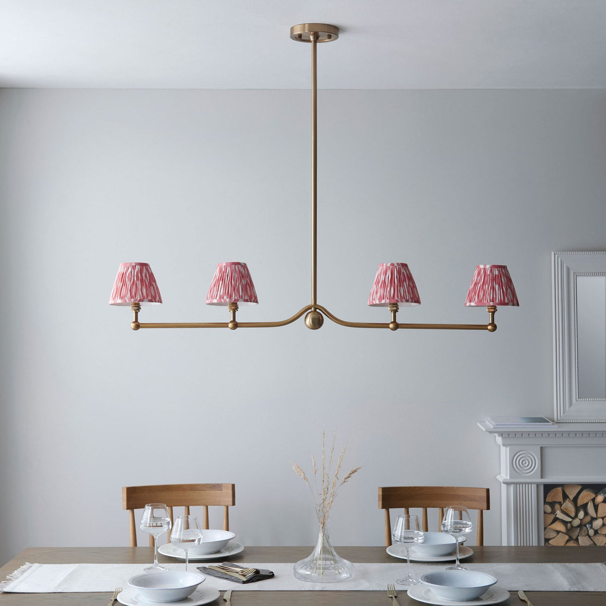 A four-light pendant with pink pleated shades above a dining table set for four.