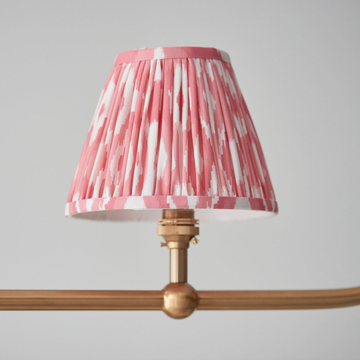 Close-up of a single pink and white patterned pleated shade on a gold light fitting.