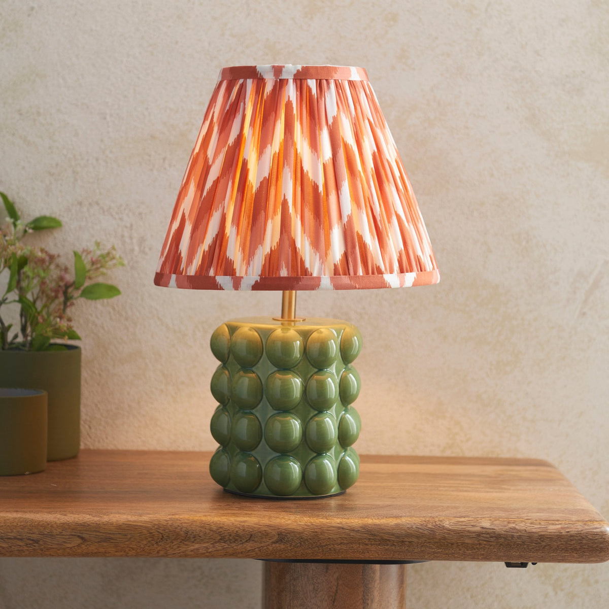 A small table lamp with an olive green ceramic base and a pleated orange and white shade.