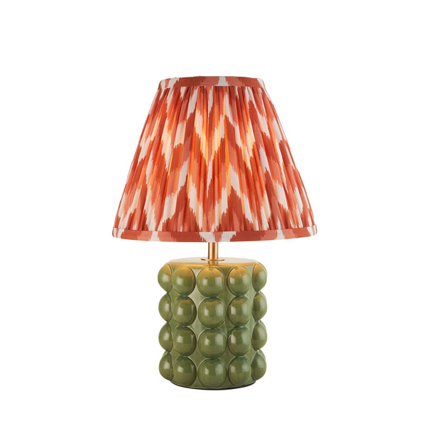 A small table lamp with an olive green ceramic base and a pleated orange and white shade.