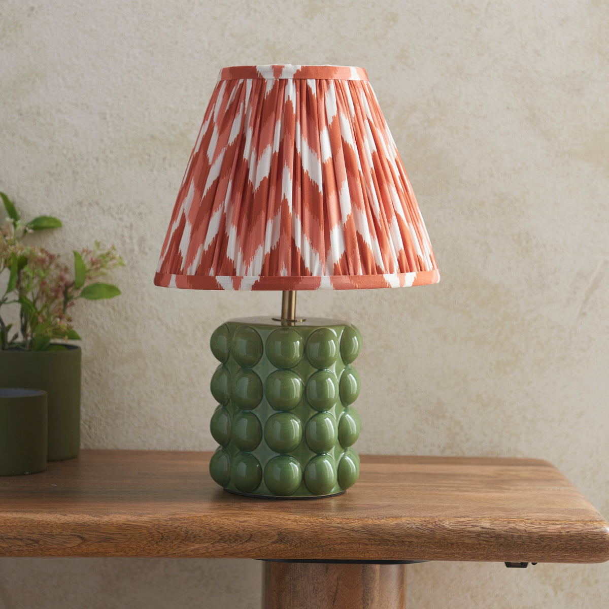 A small table lamp with an olive green ceramic base and a pleated orange and white shade.