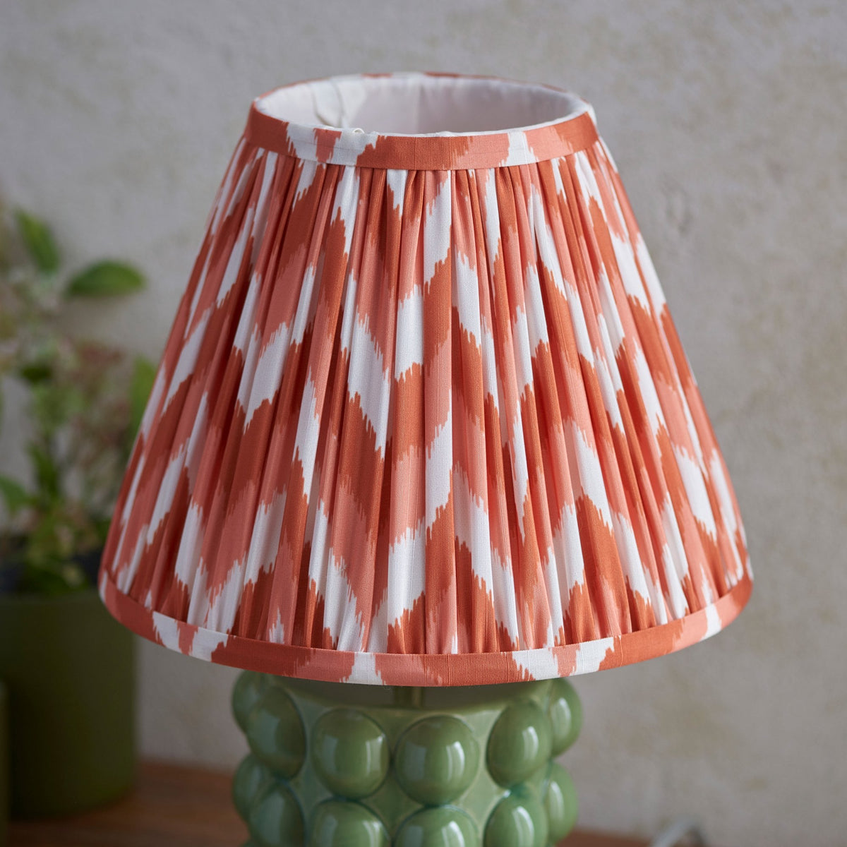 Close-up of a pleated orange and white patterned lampshade on a green ceramic base.