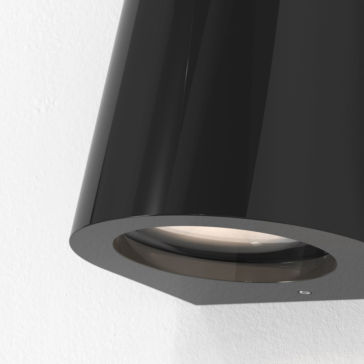 Black conical wall light with a circular opening and a warm glow against a white textured wall