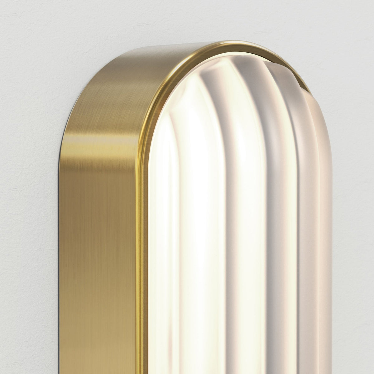 Close-up of a gold wall sconce with a fluted glass diffuser, emitting a warm glow